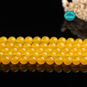 Peut inclure: Un brin de perles rondes jaunes vives, probablement en agate, disposées en rangée sur une surface noire.