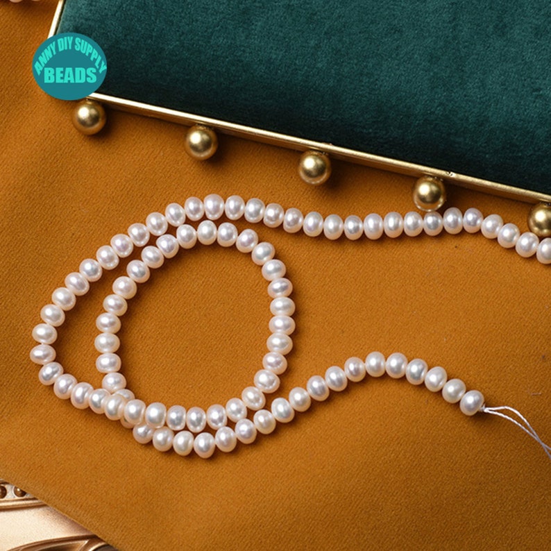 May include: A strand of white freshwater pearls, approximately 4mm in size, on a gold background. The pearls are strung on a white thread and are ready to be used for jewelry making.