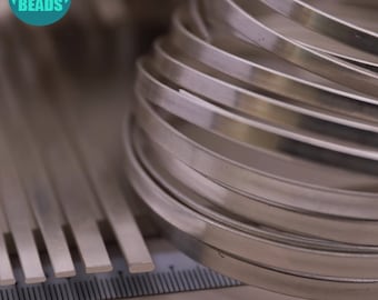 May include: A close-up of silver metal wire, some of which is coiled into circles. The wire is arranged on a ruler with markings in inches.
