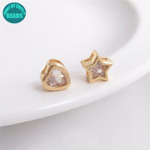 May include: Two gold-tone metal charms with clear crystal accents. One charm is shaped like a heart and the other is shaped like a star.