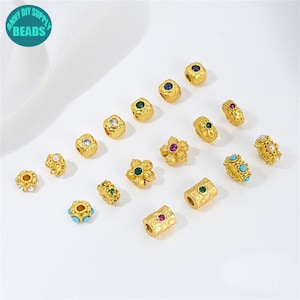 Puede incluir: Una colección de cuentas doradas en varias formas, incluyendo diseños redondos, cuadrados y florales. Algunas cuentas están adornadas con piedras preciosas de colores como azul, verde y rosa. La imagen incluye el texto "ANNY DIY SUPPLY BEADS" en un círculo turquesa.