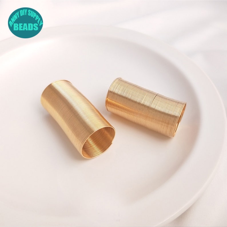 May include: Two gold-colored metal coils of wire, likely for jewelry making, are on a white plate.