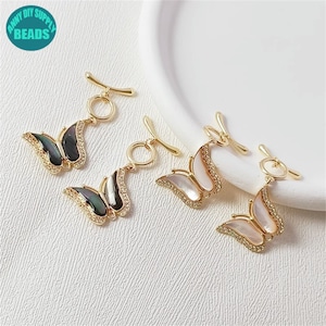 May include: Four gold-tone butterfly charms with a toggle clasp. Two charms feature a black and white shell butterfly design and two charms feature a white shell butterfly design.