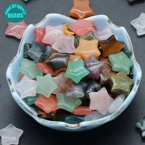 May include: A bowl filled with various star-shaped gemstone beads in shades of green, pink, brown, orange, and grey. The beads are made of natural stones like agate, tiger's eye, and rose quartz.