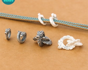 May include: Five silver dragon-shaped bead toggles. The toggles are in various sizes and shapes, with some featuring a dragon's head and others featuring a dragon's body.