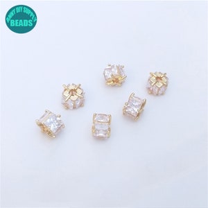May include: Six gold-toned spacers with clear cubic zirconia stones. The spacers are square shaped and have a hole in the center.
