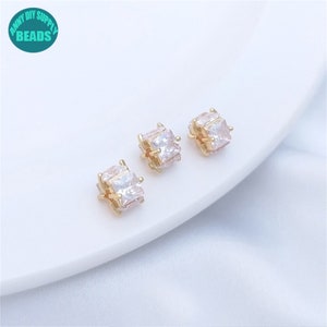 May include: Three gold-tone square-shaped earring studs with clear cubic zirconia stones.