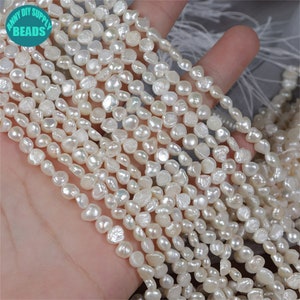 Puede incluir: Una hebra de cuentas de perlas de agua dulce blancas. Las perlas son de forma irregular y tienen un color ligeramente blanquecino. Las cuentas están enhebradas en un hilo transparente.