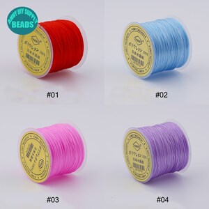 May include: Four spools of elastic string in different colours: red, light blue, pink, and purple. Each spool has a label with Japanese text and the number "100%" printed on it.