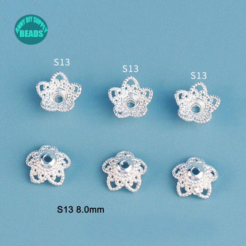 May include: Six silver-colored, flower-shaped bead caps. Each cap has a detailed, openwork design with a central hole. The text "S13 8.0mm" is visible. The caps are arranged on a light blue background. The logo "Anny DIY Supply Beads" is in the top left corner.