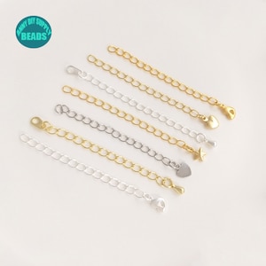 Op de afbeelding: Assortiment van gouden, zilveren en gemengde metalen kettingverlengers met verschillende bedels, waaronder harten en sterren. De verlengstukken zijn ongeveer 5 cm lang. De bedels zijn aan het uiteinde van de verlengstukken bevestigd.