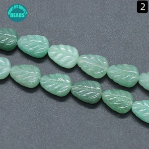 May include: A strand of light green gemstone beads, each carved with a leaf design. The beads are oval shaped and have a smooth, polished finish.