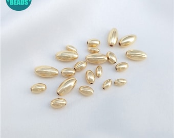 May include: A collection of gold-colored oval beads, some with a textured surface. The beads are scattered on a white surface.