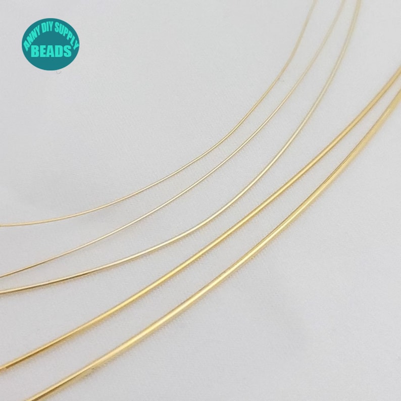 Pu&ograve; includere: Assortimento di filo color oro in diversi spessori. Il filo &egrave; disposto in un motivo curvo su uno sfondo bianco.