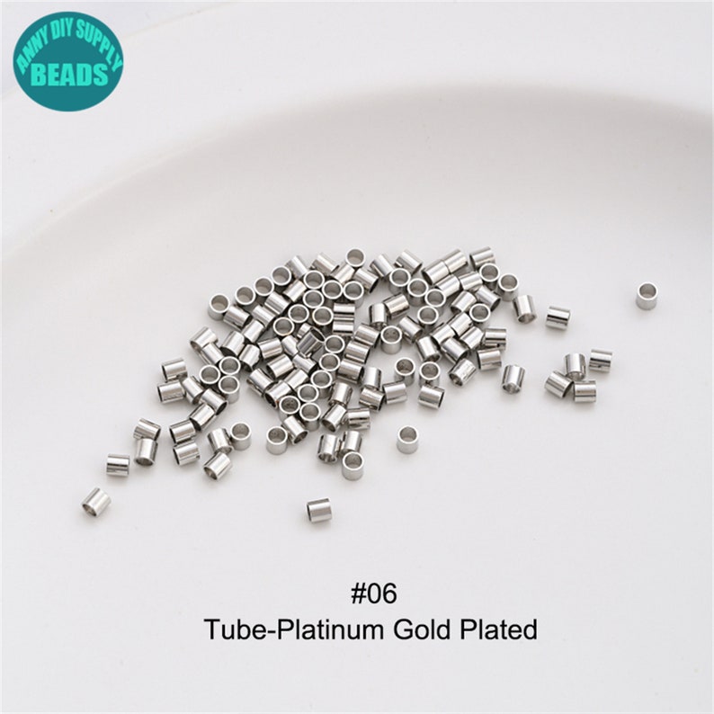 May include: A close-up of a pile of silver-toned metal tube beads. The beads are small and round, with a smooth finish. The beads are scattered on a white surface. The text "#06 Tube-Platinum Gold Plated" is printed below the beads.