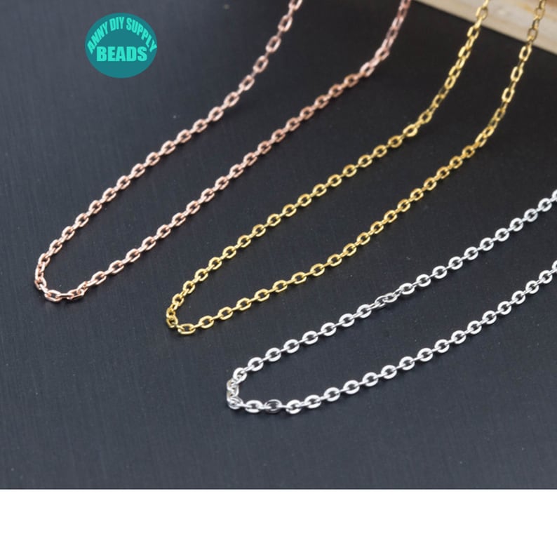 May include: Three chains in different colors: rose gold, gold, and silver. The chains are made of small oval links and are laid out on a black surface.