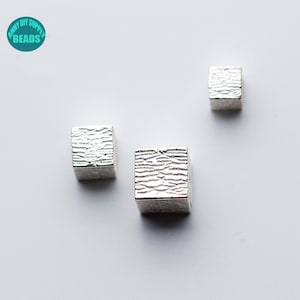 May include: Three silver metal cube beads with a textured surface.