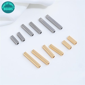 Può includere: Un assortimento di perline a tubo in metallo argentato e dorato. Le perline sono rettangolari con un'apertura quadrata ad ogni estremità. L'immagine include il testo "ANNY DIY SUPPLY BEADS".