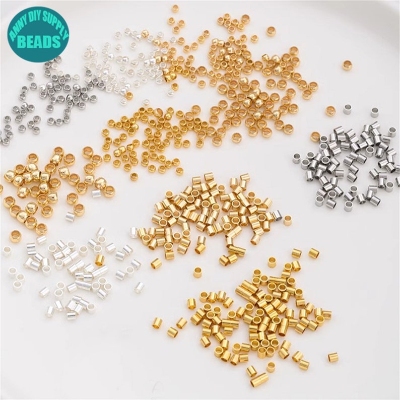 May include: Assortment of small, round, metal jump rings in silver, gold, and brass colours. The jump rings are scattered on a white surface.