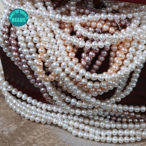 May include: A close-up of a pile of white, cream, and pink pearl beads. The beads are round and smooth, and they are arranged in a random pattern. The beads are in a wooden box with the text "ANNY DIY SUPPLY BEADS" on the front.