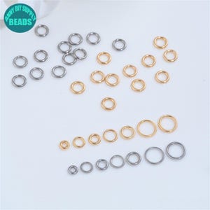 May include: A selection of gold and silver jump rings of varying sizes, scattered on a white surface. The image includes a logo that says "ANNY DIY SUPPLY BEADS". These rings are suitable for jewellery making.