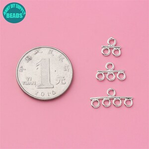 May include: Three silver-toned metal jewelry connectors with three loops each. The connectors are arranged in a row from top to bottom, with the top connector having two loops, the middle connector having three loops, and the bottom connector having four loops. A Chinese yuan coin is included for size comparison.