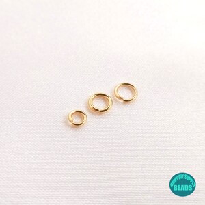 May include: Three gold jump rings of different sizes. The rings are smooth and shiny.