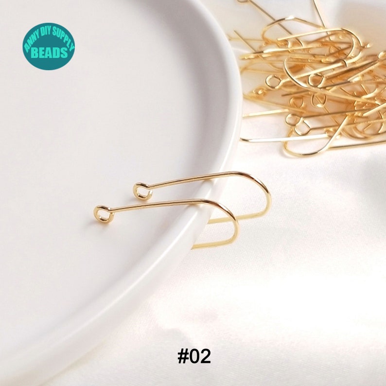May include: Two gold-toned earring hooks on a white plate. The hooks are made of metal and have a simple, elegant design. #02