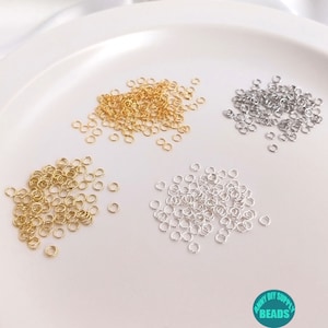 May include: Three piles of small, round, metal jump rings. The piles are on a white surface. The jump rings are gold, silver, and a lighter gold color.