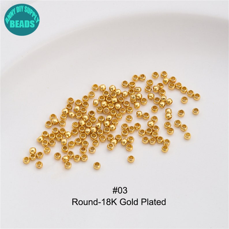 May include: A close-up image of a pile of small, round, gold-plated beads. The beads are scattered on a white surface. The text "#03 Round-18K Gold Plated" is visible below the beads.