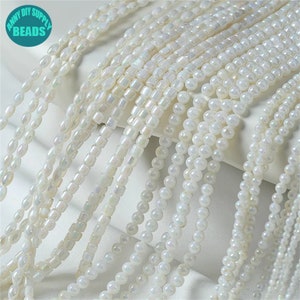 May include: Strands of white beads in various shapes, including round, square, and oval. The beads have a pearlescent sheen, reflecting light. The image includes the text "ANNY DIY SUPPLY BEADS" in a circular logo.