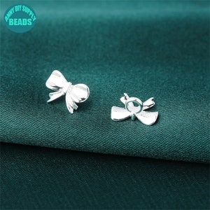 Peut inclure: Deux breloques en forme de nœud argentées, l'une avec une boucle pour l'attacher à un collier ou un bracelet, et l'autre avec un dos plat.