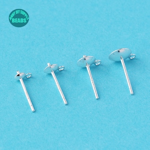 May include: Three silver earring posts with a round, flat top and a loop on the side. The posts are on a blue background.