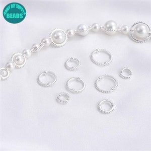 May include: A set of nine silver hoop earrings with beaded edges. The earrings are of varying sizes and are arranged on a white surface.