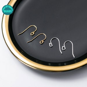 May include: Two pairs of earring hooks, one pair is gold and the other is silver. The hooks are displayed on a black plate with a gold rim.