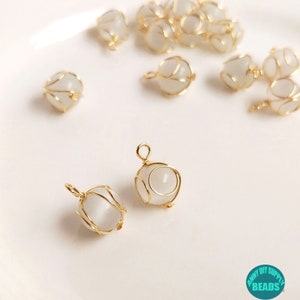 Puede incluir: Cuentas de vidrio blancas encerradas en alambre dorado, formando un diseño en forma de jaula. Las cuentas tienen una forma redonda y lisa y están enhebradas en un bucle de alambre dorado. Las cuentas son perfectas para la elaboración de joyas o manualidades.