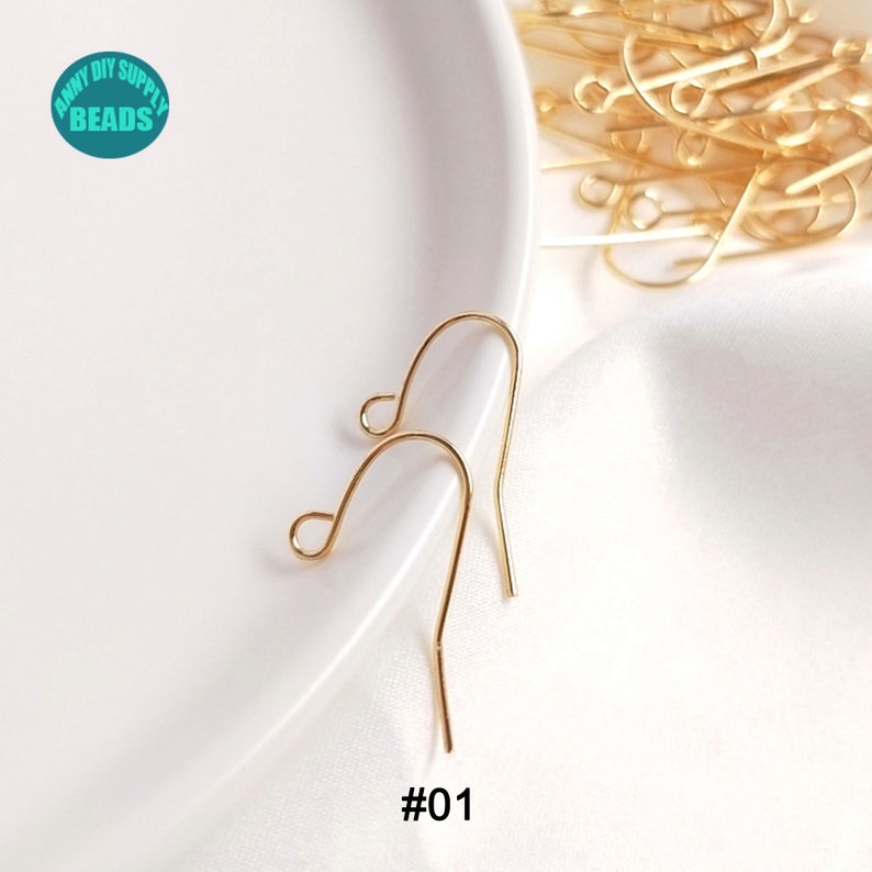 May include: Two gold-colored earring hooks on a white surface. The hooks are made of metal and have a simple design. #01