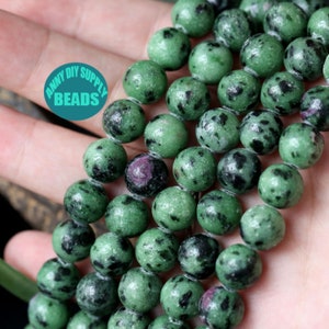 Puede incluir: Una hebra de cuentas de piedras preciosas verdes y negras. Las cuentas son redondas y tienen un aspecto moteado.