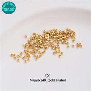 May include: A close-up image of a pile of small, round, gold-plated beads. The beads are scattered on a white surface. The text "#01 Round-14K Gold Plated" is visible below the beads.