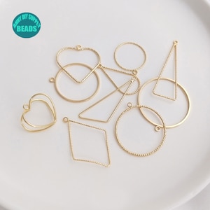 Puede incluir: Un conjunto de nueve piezas en blanco para pendientes de metal dorado en varias formas, incluyendo círculos, corazones y triángulos. Las piezas en blanco tienen aproximadamente 5 cm de tamaño y un acabado texturizado.