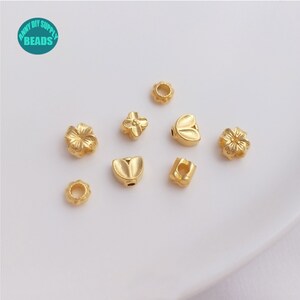 May include: Assortment of gold-toned metal beads with various designs, including flowers, leaves, and a heart. The beads are small and have a shiny finish.