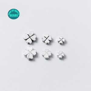 May include: Six silver four-leaf clover charms of varying sizes. The charms are made of metal and have a shiny finish.