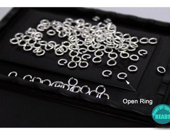 May include: A close-up of a black tray filled with silver open jump rings. The text "Open Ring" is visible in the lower right corner of the image.