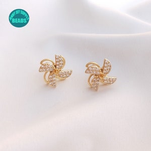 May include: A pair of gold earrings with a windmill design. Each earring is adorned with clear rhinestones.