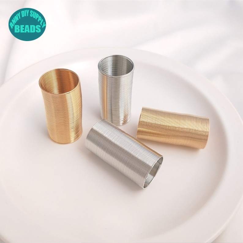 May include: Four spools of metal wire, two gold and two silver, on a white plate. The wire is coiled tightly and is ready to be used for crafting.