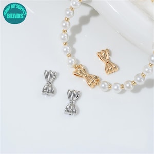 May include: An image of jewelry making supplies. The image shows a pearl bracelet with gold accents and two gold bow-shaped clasps. There are also two silver bow-shaped clasps. The image has a white background and a teal circle with the words "ANNY DIY SUPPLY BEADS".
