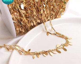 May include: Gold chain with small, dangling leaf-shaped charms. The chain is wound around a spool and a portion of the chain is laid out on a white surface.