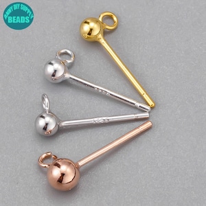 Puede incluir: Primer plano de cuatro postes de pendientes en oro, plata y oro rosa. Cada poste tiene una pequeña bola en la parte superior y un lazo para sujetar un dije. Los postes están sobre una superficie gris. En la esquina superior izquierda hay un círculo turquesa con las palabras "FUNNY DIY SUPPLY BEADS".