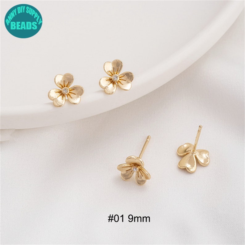 K&ouml;nnte beinhalten: Drei Paar goldfarbene Ohrstecker in Blumenform mit einem einzelnen klaren Strassstein in der Mitte jeder Blume. Die Ohrringe sind 9 mm gro&szlig; und mit #01 9 mm gekennzeichnet.