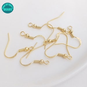 May include: Gold-toned earring hooks with a spring and a small ball at the end. The hooks are arranged in a pile on a white surface.
